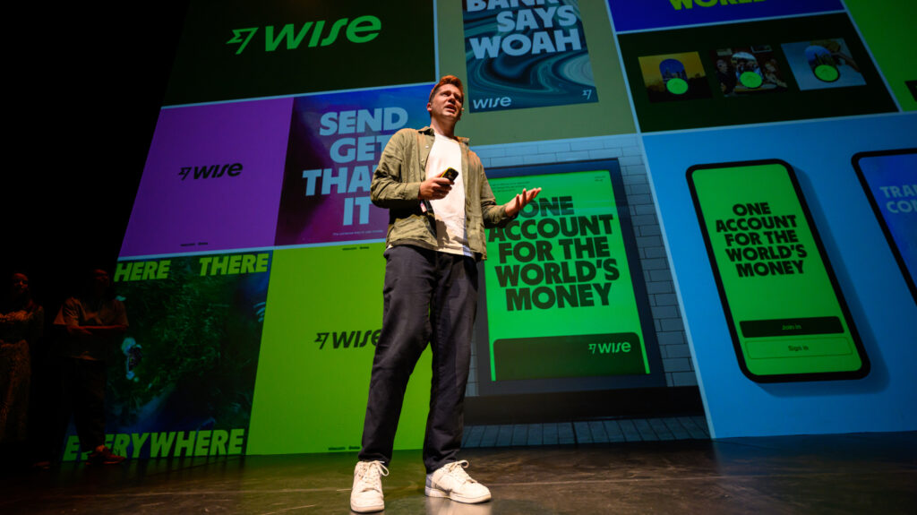 POV Budapest - Egy előadó beszél a színpadon, háttérben színes grafikai elemekkel és szövegekkel a Wise márkától.
